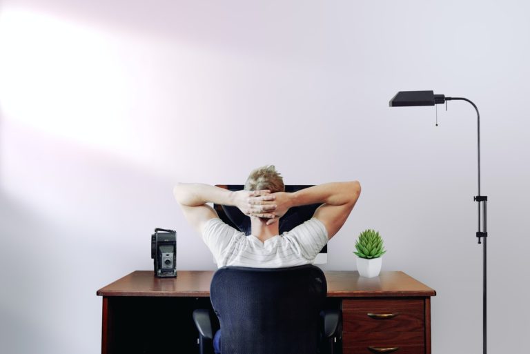 A person sitting in front of the computer holding its head with hands.
