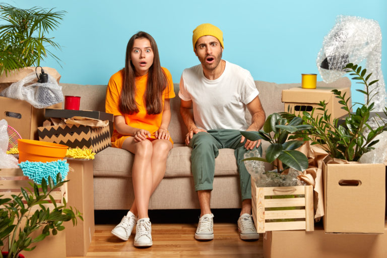 Emotional two shocked woman and man stare with bugged eyes, surprised by high price of renting new flat, sit on couch together, have conversation with real estate. Welcome to new home concept
